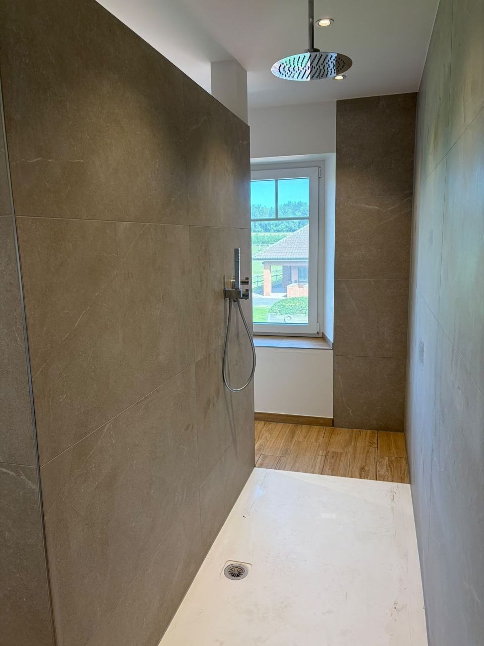 Bodengleiche Dusche mit Regenbrause, Wände im Steinoptik-Großformat, Blick durchs Fenster ins Grüne